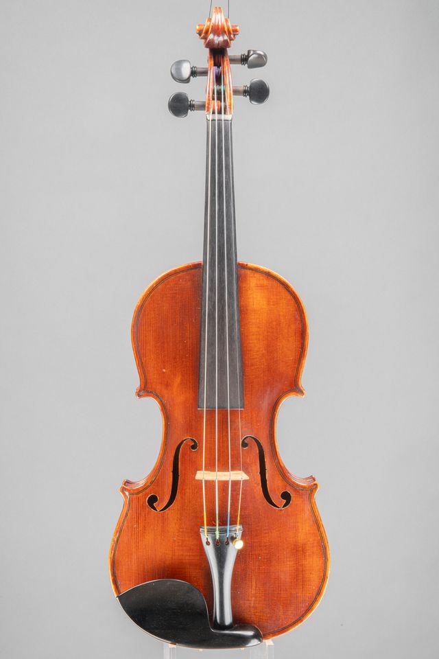 A studio portrait of a classic wooden violin, characterized by its deep, dark amber finish, set against a simple, neutral gray backdrop.