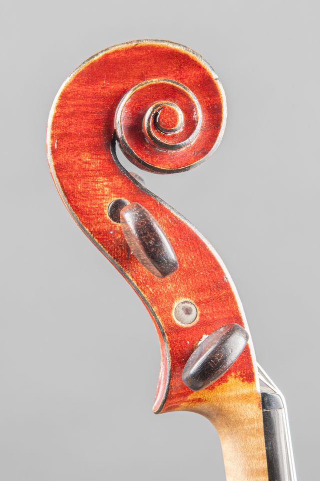 A close-up view of a wooden violin scroll and tuning pegs against a neutral grey background.