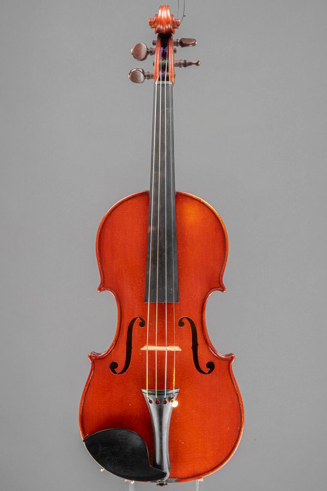 A studio shot of a classic wooden violin, captured from the front against a solid grey background.