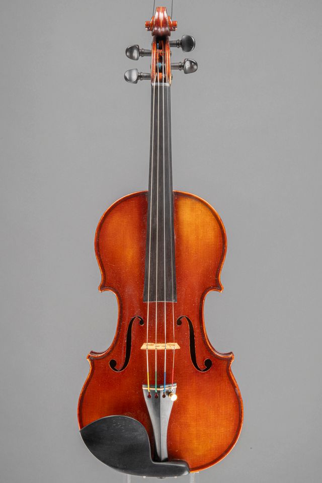 A frontal studio photograph of a classic wooden violin, displayed against a plain grey background.