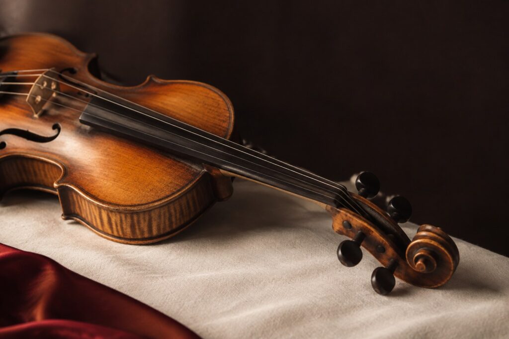 Early 20th-century Milanese violin with amber varnish resting on an ivory surface in warm window light against a dark background